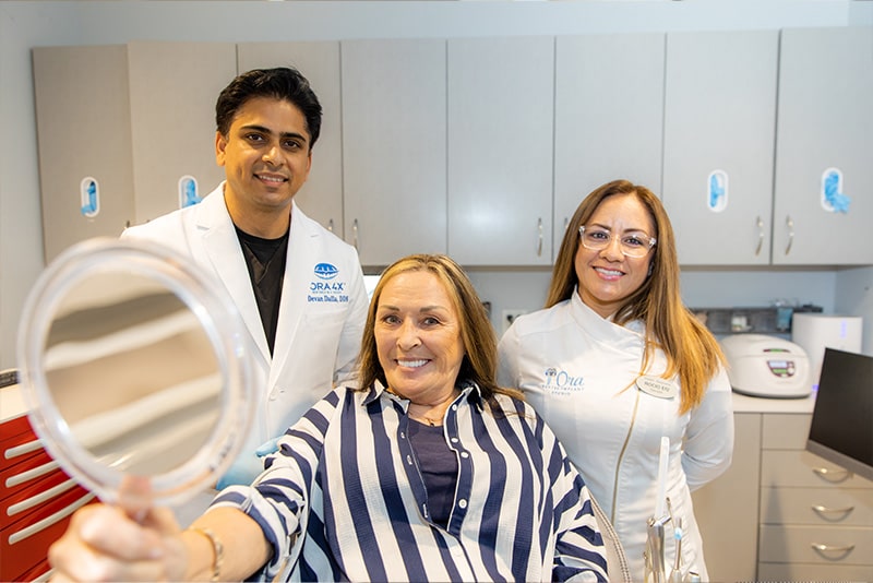 Dr. Dalla with his dental assistant and patient holding a mirror