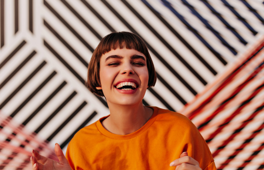 Person in an orange shirt smiling in front of a geometric, striped background.