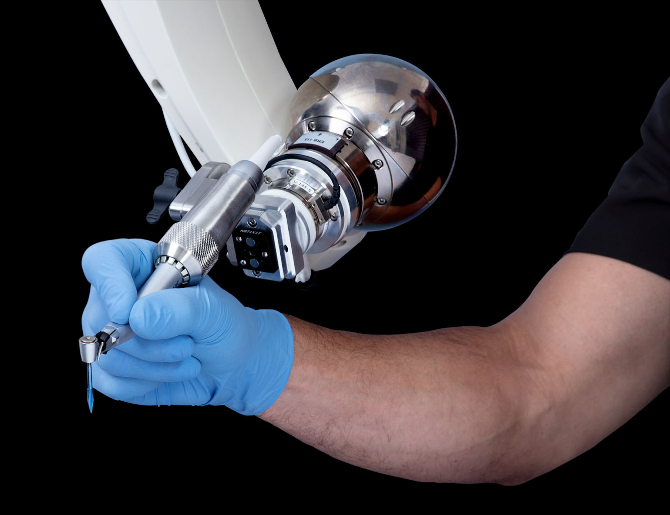 A person wearing a blue medical glove operates a handheld device attached to a large, metallic, spherical medical machine.