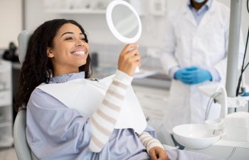 Smiling dental patient checking her teeth in a mirror during a consultation before implant surgery.
